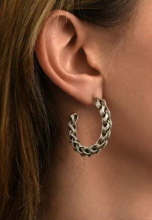 Des boucles d'oreilles en argent présentent un design tressé avec des détails complexes. La texture est lisse avec une finition polie.