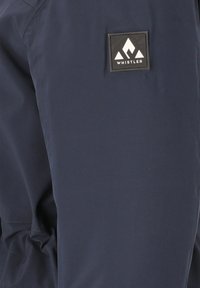 Marineblaue Outdoor-Hosen mit glatter Textur, ausgestattet mit einem schwarzen rechteckigen Logo-Patch mit einem weißen Bergdesign.
