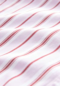 Tessuto di cotone con strisce diagonali rosa e rosse su fondo bianco, caratterizzato da una texture liscia e una leggera lucentezza.