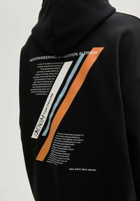 Zwarte hoodie met een grafisch ontwerp met oranje en blauwe strepen. Tekst op de achterkant beschrijft bergbeklimmen en gerelateerde activiteiten.