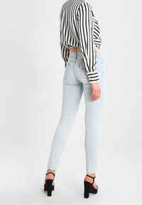 Jeans ajustados de un azul claro, hechos de denim, con una cintura alta y un sutil desvanecimiento. Combinados con una blusa corta de rayas en blanco y negro y tacones altos.