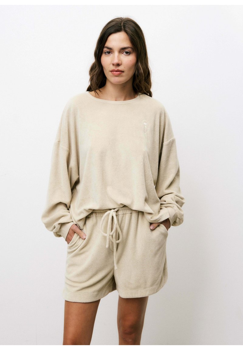Beige fleece lounge set met een oversized top met lange mouwen en korte broek met trekkoord en zijzakken. Getextureerde stof met een subtiele glans.