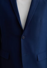 Giacca da abito blu navy con rever a punta, due bottoni e tasche a filetto. Tessuto liscio con texture sottile e dettagli di cucitura a contrasto.