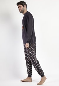 Conjunto de ropa de estar en casa para hombre que incluye una camiseta de manga larga en gris oscuro y pantalones de piyama negros con un estampado floral colorido. Tela suave, puños elásticos.
