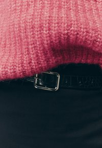 Rosa stickad tröja med ett texturerat mönster, parat med ett svart läderbälte med krokodilsmönster och en silvrig metallspänne.