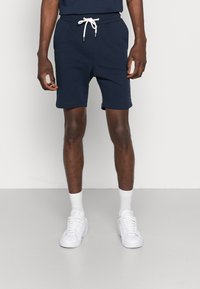 Shorts en mélange de coton bleu marine avec une taille élastique et un cordon de serrage blanc. Dotés de poches latérales et d'une coupe slim. Associés à des baskets blanches et des chaussettes.