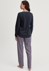 Marineblaues Langarmoberteil mit einem gemusterten Ausschnitt, kombiniert mit karierter Schlafanzughose in Marineblau, Weiß und Rot. Aus weichem Baumwollmaterial.