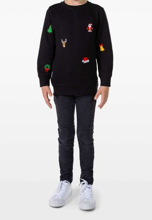 Czarna bluza z różnokolorowymi naszywkami o tematyce świątecznej, w tym Mikołaj, choinka, jeleń, wieniec i dzwonek. Stylizowana z dżinsami i trampkami.
