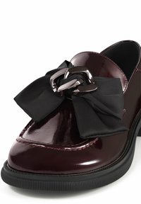 Bordeaux patentleren schoen met een brede zwarte satijnen strik en een metallic kettingaccent. Heeft een ronde neus en een gestructureerde zwarte zool.