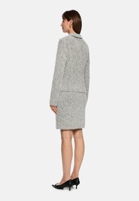 Helles graues, strukturiertes Jacken- und Rock-Set mit Kragen und tailliertem Schnitt. Getragen mit schwarzen spitzen Absatzschuhen.