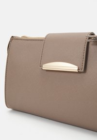 Borsa a tracolla in pelle taupe testurizzata con una chiusura semicircolare in tonalità oro e una tracolla in catena dorata parzialmente visibile su uno sfondo bianco.