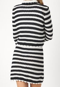 Černobílé proužkované šaty s texturovaným pleteným vzorem. Mají vykrojený lem a límeček. Střední délka.