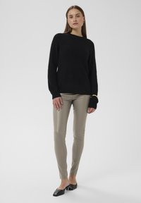 Pull noir texturé à manches longues, associé à un pantalon ajusté en similicuir beige clair et des mules noires à bout carré.