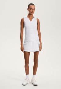 Bela brezrokavna polo majica z V-izrezom, teksturirana tkanina, v kombinaciji z ujemajočo belo krilo s stranskim razporkom in kontrastnim robom.