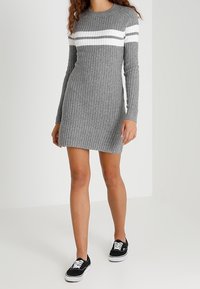 Grå ribbade stickade klänning med vita horisontella ränder, rundad halsringning, långa ärmar, mitt-lår längd, tillsammans med svarta sneakers.