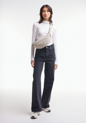 Bolso de hombro acolchado beige llevado sobre una blusa blanca de manga larga, combinado con jeans negros de cintura alta y zapatillas blancas.