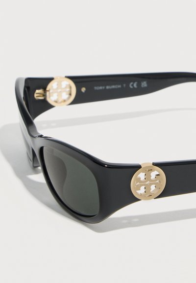 Μαύρα μεγάλα γυαλιά ηλίου με σκουρόχρωμους φακούς και χρυσά στρογγυλά διακοσμητικά με λογότυπο στα πλαινά μέρη.