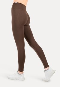 Brązowe legginsy z wysokim stanem, gładką fakturą i dopasowanym krojem, w połączeniu z białymi butami sportowymi.