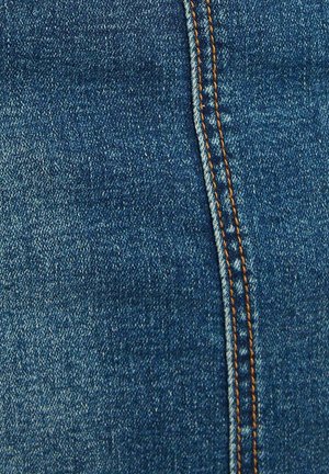 Tela de denim azul oscuro con una costura visible que presenta un ribete naranja y una superficie ligeramente texturizada, exhibiendo un material clásico de pantalón vaquero.