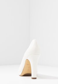 Bílá vysoká podpatková bota otočená dozadu, ukazující hladký kožený povrch, tenký podpatek a velikostní označení na podrážce.