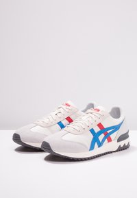 Sneakers bianchi con strisce rosse e blu, punte in suede e suole in gomma testurizzata. Design con lacci e colletto imbottito.