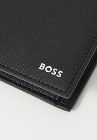 Black textured wallet made of synthetic material, featuring a stitched edge and a white "BOSS" logo on the front.