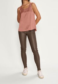 Rosa ärmfri topp med slät yta, i kombination med figurnära bruna leggings och vita sneakers. Enkelt design med minimala detaljer.