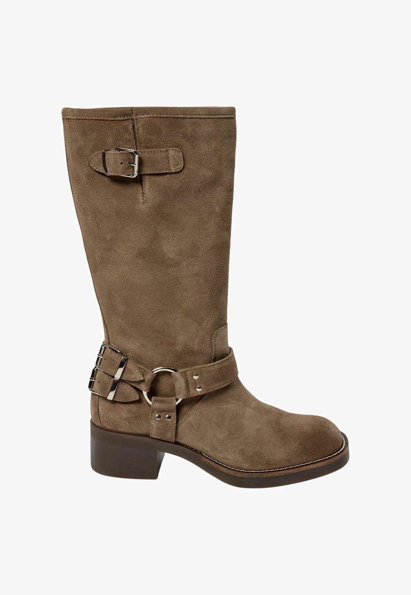 Brūni zamšādi ceļa augstuma zābaki ar noapaļotu purngalu, zemu kvadrātveida papēdi un divām regulējamām sprādzēm sānos. Akcentēti ar metālisku aparatūru.