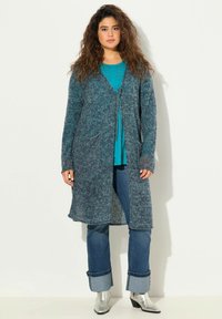 Lång, öppen cardigan i en strukturerad, blå stickning med två framfickor. Matchad med en teal-top, jeans och silverfärgade ank stövlar.