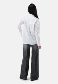 White long-sleeve shirt with a back pleat, worn with high-waisted black wide-leg jeans featuring subtle fading and a raw hem.