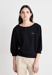 Felpa nera con scollatura ampia e maniche a sbuffo. Presenta un ricamo rosa con la scritta "Boss" sul petto. Tessuto in cotone morbido e strutturato.