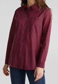 Camicia a maniche lunghe con bottoni di colore rosso, decorata con un motivo circolare blu e bianco. Realizzata in tessuto morbido, presenta un colletto e una vestibilità comoda.