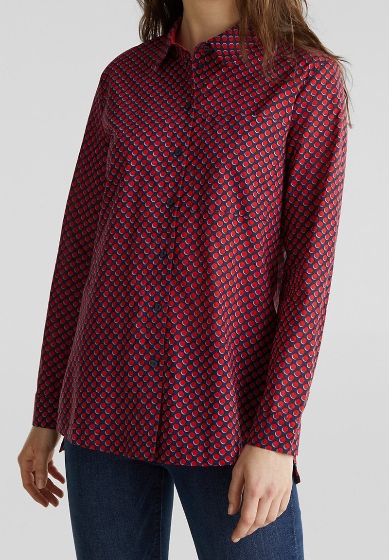 Camicia a maniche lunghe con bottoni di colore rosso, decorata con un motivo circolare blu e bianco. Realizzata in tessuto morbido, presenta un colletto e una vestibilità comoda.