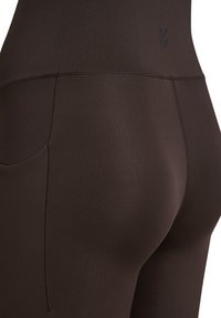 Bruine legging met hoge taille gemaakt van gladde stof, met een subtiele textuur en een zakdetail aan de zijkant. Minimalistische ontwerpaccenten.