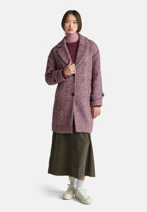 Haringbone-patroon jas in bordeaux en wit, met een geknipte kraag, twee knopen en een ontspannen pasvorm, gedragen over een paarse turtleneck en een groene rok.