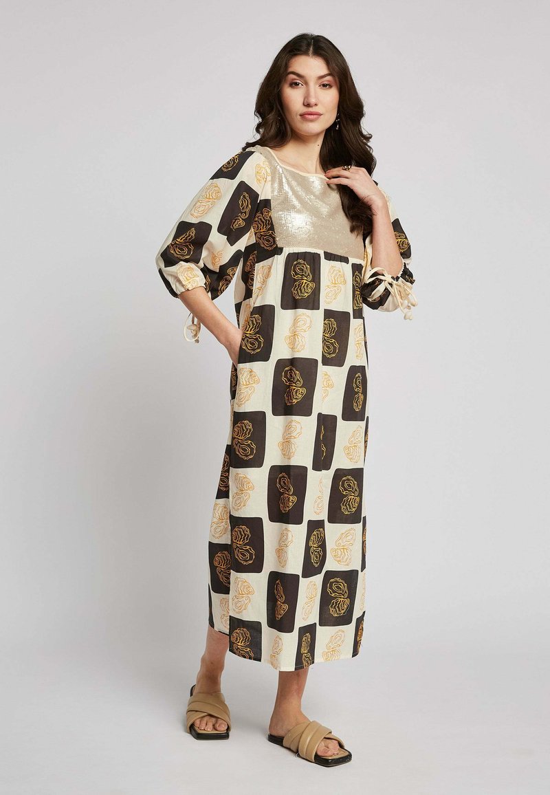 Maxikleid mit einer crèmefarbenen Basis, braunen und gelben Blumenmustern, kurzen Puffärmeln und einem glänzenden goldenen Akzent am Oberteil.