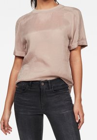 Camicia rosa chiaro a maniche corte in tessuto morbido con risvolti, abbinata a jeans denim scuri con trama sottile e tasche classiche.