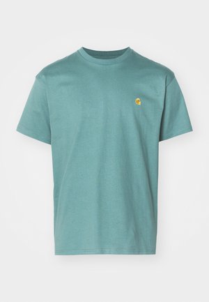 Bomulds T-shirt i teal, korte ærmer, rund halsudskæring, med et lille gult logo på venstre bryst. Textureret stof med en glat overflade.