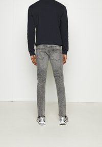 Jeans gris ajustados con un acabado desgastado, bolsillos traseros y detalles. Combinados con una camiseta negra de manga larga y zapatillas deportivas plateadas.
