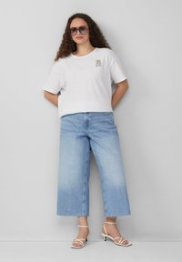 T-shirt en coton blanc avec un graphique "C'est tout bon". Assorti à un jean en denim large et bleu clair, et des talons strappy blancs.
