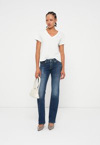 T-shirt blanc à col en V, jeans droits bleus, escarpins gris à bout pointu et petit sac à main blanc. Tissu lisse, coupe décontractée et design simple.