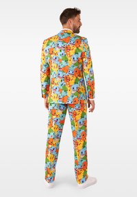 Multikleurig pak met een levendig patroon van stripfiguren in blauw, groen en oranje. De stof lijkt soepel en op maat gemaakt.