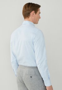 Camicia azzurro chiaro a maniche lunghe con colletto classico, realizzata in tessuto testurizzato. Abbinata a pantaloni grigi con tasca posteriore e bottone.