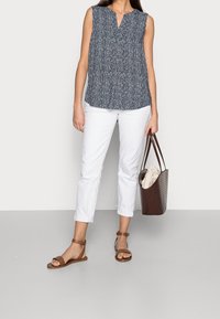 Haut sans manches bleu marine avec un motif texturé blanc, associé à un pantalon blanc aux chevilles. Sac en cuir tressé marron et sandales marron avec des brides à la cheville.