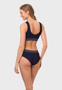 Navy blue sports bra and high-waisted bikini bottom with contrasting horizontal stripes on the band. Smooth texture and fitted design.