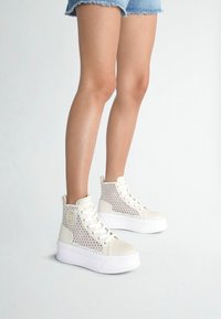 Witte hoge sneakers met mesh-details, stevige neusbescherming en een dikke witte zool. Bevat een logo-patch aan de zijkant en vetersluiting.