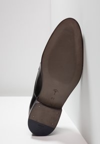 Suela de zapato de cuero negro con superficie texturada, impronta de logo, tamaño 41 y tachuelas doradas; forma curva con tacón distintivo.
