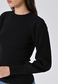 Schwarzer Strickpullover mit langen, strukturierten Ärmeln und einem gerippten Design. Figurbetonter Schnitt mit rundem Halsausschnitt und gerippten Bündchen.