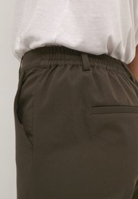 Pantaloni elasticizzati marrone scuro con design casual, dotati di tasche laterali e una Texture liscia, abbinati a una maglietta grigio chiaro.