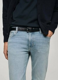 Marineblauwe cardigan over een zwart T-shirt, gecombineerd met lichtblauwe spijkerbroek. Zwarte leren riem met zilveren gesp. Subtiele textuur in de spijkerbroek.